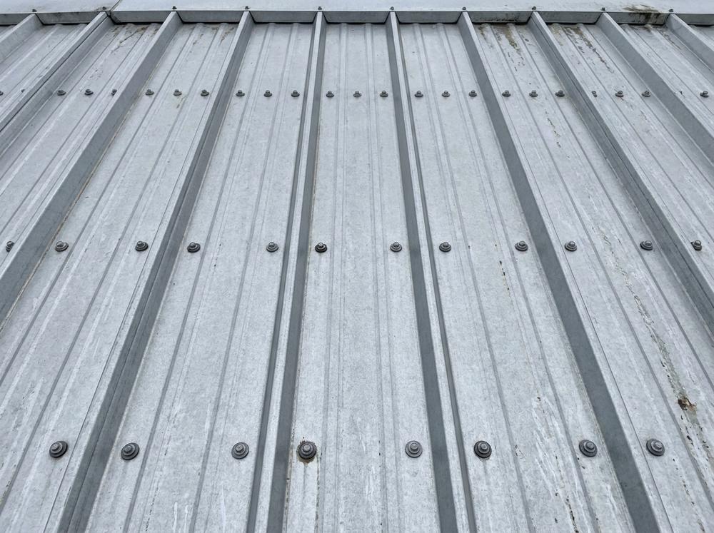 Ribbed metal roof with screws fastened through the flat pan between raised ribs