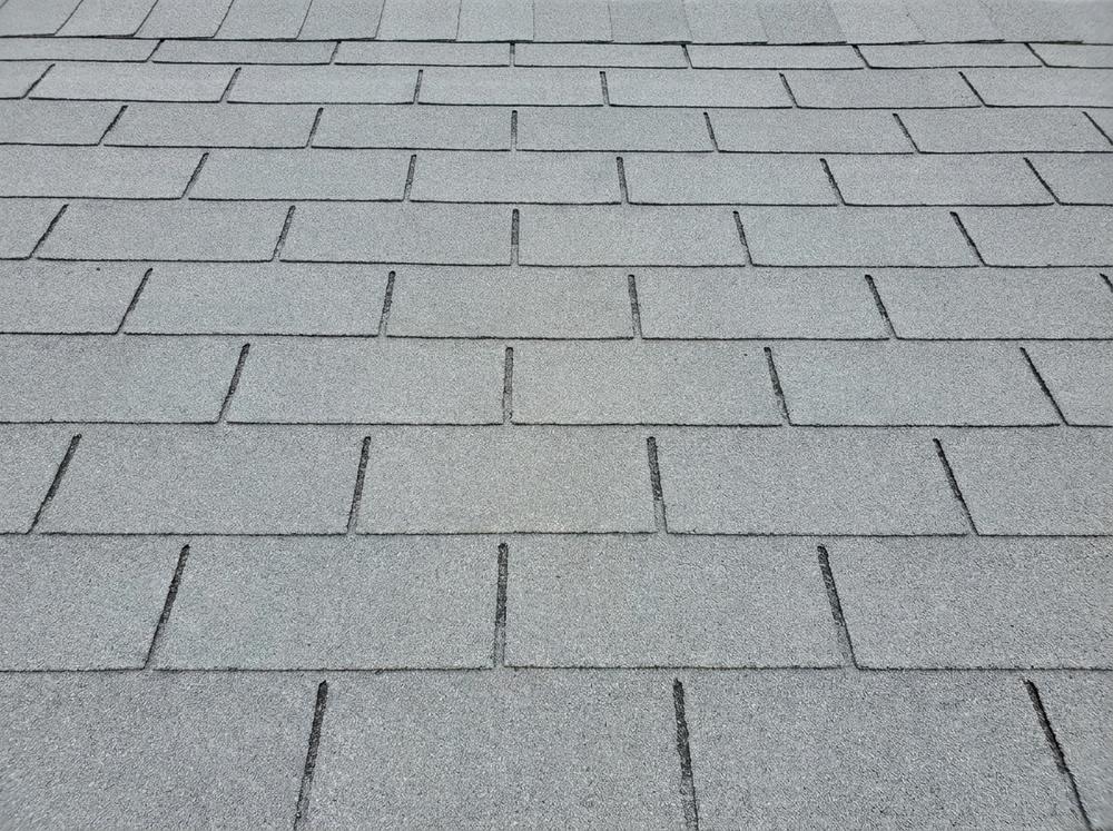 Close-up of a grey three-tab asphalt shingle roof showing flat uniform tabs